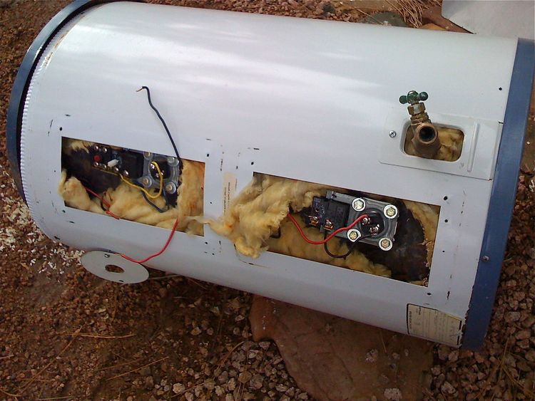 An electric geyser with its covers off, showing two elements, their thermostats and the brass drain cock